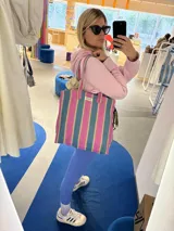 Bolso tipo tote bag con estampado a rayas verticales en tonos verde, rosa, celeste y marrón. Tiene asas de hombro y un parche con la inscripción "AMÉN".