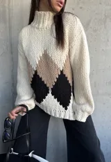 Sweater de punto grueso con cuello alto, diseño de rombos en tonos beige y negro sobre base color natural, de corte holgado y mangas largas con puños ajustados.