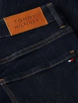 Jeans de calce ajustado color azul oscuro, con diseño de cinco bolsillos, cierre de botón y cremallera, detalles distintivos de Tommy Hilfiger y logo sobre el bolsillo posterior.