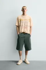 Camiseta relaxed fit de punto color beige con efecto lavado, cuello redondo y manga corta. Cuenta con estampado frontal con texto en tonos amarillo, azul y rojo.