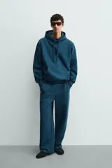 Pantalón jogger de corte relajado y pernera ancha, confeccionado en tejido de algodón con interior perchado. Presenta cintura elástica con cordón interior, bolsillos laterales y un bolsillo trasero de plastrón.