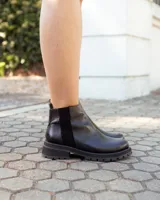 Botinetas de cuero negro con suela track dentada. Presentan un diseño de caña baja con paneles laterales elásticos y cierre lateral, combinando texturas de cuero liso y texturizado.