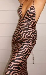 Vestido largo de satén con estampado de cebra en tonos marrón claro y negro. Presenta un escote pronunciado en V con tirantes finos ajustables en la espalda.