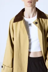 Trench color beige con cuello camisero, doble botonadura frontal, cinturón y bolsillos laterales.