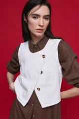 Chaleco de denim blanco con diseño cruzado, escote redondo y cierre frontal con botones carey.
