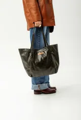 Cartera de cuero color verde oscuro, tipo tote bag, con asas dobles y una etiqueta de marca en cuero marrón claro en el frente.