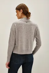 Polera de lana y cachemira color gris, con cuello alto y mangas largas con textura acanalada. Presenta un diseño holgado con aberturas laterales en el ruedo.