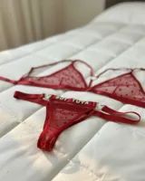 Conjunto de lencería de dos piezas en tul rojo con patrón de corazones y detalles de argollas en forma de corazón. Incluye un bralette triangular con tirantes ajustables y una tanga con la frase "Soy Tuya" aplicada en strass.