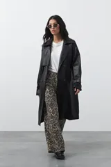 Trench coat de símil cuero color marrón oscuro, con solapas amplias, cierre frontal con botones, cinturón ajustable en la cintura y mangas con tiras ajustables. Presenta un largo por debajo de la rodilla y bolsillos laterales.