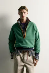 Sudadera regular fit color verde con cuello subido y cierre frontal de cremallera corta en tono naranja a contraste. Cuenta con mangas largas raglán, bolsillos frontales tipo canguro y puños y cintura en canalé de color azul marino.
