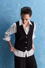 Chaleco negro con escote en V, cierre frontal con botones y bolsillos ribeteados simulados.