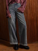 Pantalón de jean wide leg color azul medio con efecto gastado, tiro alto y costuras laterales decorativas que recorren toda la pierna. Presenta corte recto y pierna ancha con bolsillos funcionales.