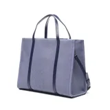 Cartera grande tipo tote bag de textura denim con detalles en cuero sintético azul oscuro. Cuenta con doble asa de mano, correa ajustable para el hombro y un bolsillo frontal con cierre y el logo de la marca Extra Large.