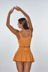 Conjunto deportivo compuesto por un top de escote redondo con logo estampado y una pollera short con tablas. Diseño en color naranja, confeccionado en tejido elástico de secado rápido.