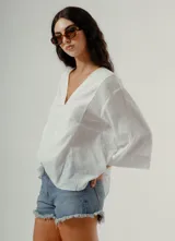 Blusa blanca de manga tres cuartos con cuello en V y textura sutil, corte holgado.