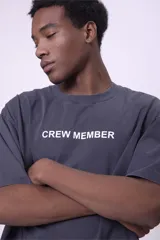 Camiseta de manga corta, color gris oscuro con efecto lavado, corte oversize y cuello redondo. Presenta un pequeño estampado en el pecho con el texto "CREW MEMBER" en blanco.