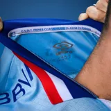 Camiseta de fútbol Umbro del Club Nacional de Football, modelo Away 3. Diseño en color celeste con detalles en azul, blanco y rojo en el cuello y los puños. Incluye logo de Umbro, escudo del club y sponsors estampados en el frente y laterales.