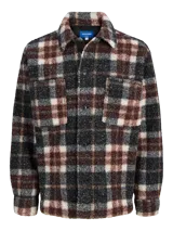 Sobrecamisa de textura tipo teddy con estampado de cuadros en tonos marrón, negro y crema. Presenta cuello camisero, cierre frontal de botones, bolsillos en el pecho y puños abotonados, con un corte relajado.