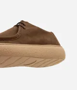 Championes de estilo casual con diseño moc toe, confeccionadas en cuero gamuza color marrón. Presentan costura visible en la puntera, cierre con cordones y suela de goma en tono beige de perfil bajo.