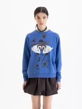 Buzo de cuello redondo y manga larga, color azul con estampa frontal de cisnes y flores. Presenta un calce amplio y largo a la cadera.