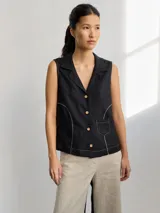 Camisa sin mangas de corte sastrero, color negro, con cuello solapa y cierre frontal con botones. Presenta costuras decorativas en contraste y un pequeño bolsillo frontal.