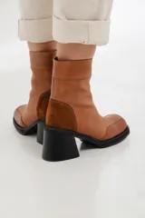 Bota corta de cuero color suela, con diseño de paneles en gamuza al tono en el talón. Presenta un taco cuadrado robusto de color negro y punta cuadrada.