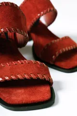 Sandalias tipo mule de taco medio, confeccionadas en cuero gamuzado color terracota. Presentan dos tiras anchas con detalles de costuras pespunteadas en los bordes y taco cuadrado estable.