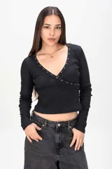 Remera negra de manga larga con escote en V cruzado y detalle de tachas plateadas a lo largo del borde del escote.