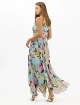 Vestido largo de chifón con estampado floral, cuello halter con pliegues y abertura tipo lágrima. Presenta una cintura drapeada que estiliza la silueta y una falda amplia con capas asimétricas y bajo en picos. Incluye forro interior y cierre invisible en la espalda.