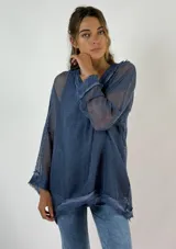 Top azul de malla calada con cuello en V y mangas largas acampanadas. Presenta detalles de terminación desflecada en cuello y ruedo.