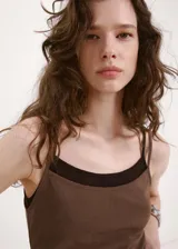 Vestido corto marrón con efecto de doble prenda, superpuesto sobre un fondo negro. Presenta tirantes finos y un diseño ajustado al cuerpo con fruncidos en los laterales.