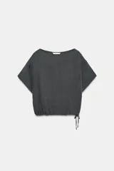 Camisa amplia de manga corta y cuello redondo, color gris oscuro, con diseño estilo capa y bajo ajustable con lazada lateral.