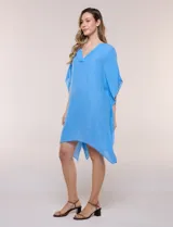 Vestido playero tipo túnica de corte holgado color rosado, confeccionado en tejido semi transparente con textura sutilmente arrugada. Cuenta con escote en V pronunciado, mangas estilo kimono de caída fluida y aberturas laterales en el ruedo irregular.