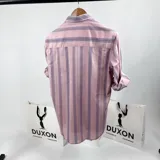 Camisa de vestir de manga larga, color rosa con rayas verticales en tonos de gris y blanco. Tiene cuello italiano, cierre con botones y logo bordado en el pecho.