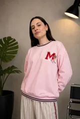 Buzo de cuello redondo color rosa, con diseño holgado y mangas largas. Presenta un aplique bordado en el pecho con la letra M y detalles de rayas negras en el cuello y el ruedo.