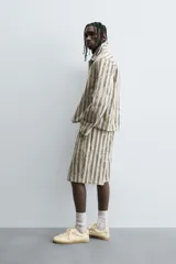 Cazadora de hombre de corte relajado, color beige claro con rayas verticales en azul oscuro con efecto desgastado o estampado. Presenta cuello solapa, manga larga, bolsillos de vivo en cadera y cierre frontal con botones a presión.