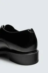 Zapato de vestir tipo derby de cuero negro brillante, con cordones y suela con ligero tacón.