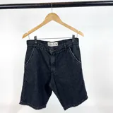 Bermuda de jean negro con detalle de rotura en el bolsillo y costuras a la vista.