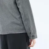 Sobrecamisa de corte recto y diseño estructurado, confeccionada en tejido gris con patrón de rayas verticales finas. Presenta cuello clásico, cierre frontal con botones y dos bolsillos frontales con solapa.
