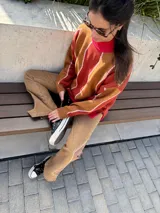 Sweater de punto con cuello alto, diseño geométrico con rayas diagonales en tonos naranja, marrón y blanco.