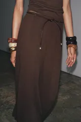 Falda larga de tiro medio, color beige claro, con caída amplia y cinturón fino negro anudado en la cintura.