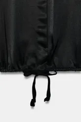 Camisa de satén con cuello solapa, manga larga con puños y bajo ajustable mediante cordones. Presenta cierre frontal con botones ocultos.