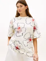 Remera de manga corta Tommy Hilfiger de corte relajado, color blanco con estampado floral de contornos azul oscuro y detalles en rojo. Presenta cuello redondo y diseño holgado.