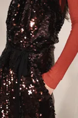 Vestido largo de lentejuelas con cuello halter, espalda descubierta y lazos para atar al cuello. Cuenta con un cinturón de lazo en contraste y diseño bicolor que combina tonos tostados y negros.