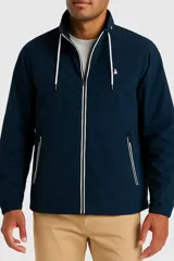 Campera tipo rompevientos color azul marino con cierre frontal completo, cuello alto y capucha oculta. Presenta detalles en color blanco en el cierre, cordones de la capucha y bordes de los bolsillos laterales. Incluye el logo de la marca bordado en el pecho.