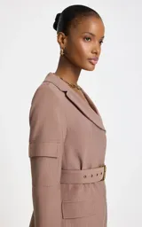Blazer sastre color marrón claro con patrón de raya diplomática, cuello con solapa ancha, mangas largas con bolsillos aplicados en las mangas, bolsillos frontales con solapa, cinturón incorporado con hebilla metálica y cierre cruzado.