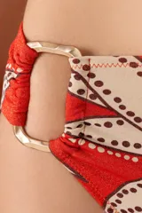 Calzón de bikini tiro alto con estampado floral en tonos naranja, beige y marrón. Presenta un aro dorado en el lateral.