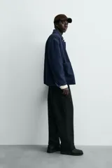 Chaqueta de denim de algodón en color azul oscuro con corte relaxed fit. Presenta cuello de solapa, cierre frontal con botones metálicos y tres bolsillos de parche en el delantero. Las mangas son largas con puños abotonados.