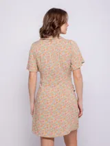 Vestido corto de viscosa con estampado floral multicolor, de manga corta, con cuello camisero y cierre frontal abotonado. Presenta un nudo decorativo en la cintura.
