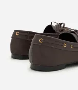 Mocasín dockside de cuero color marrón, con costuras aparentes, cordones frontales con lazo, ojetes metálicos dorados y suela baja.